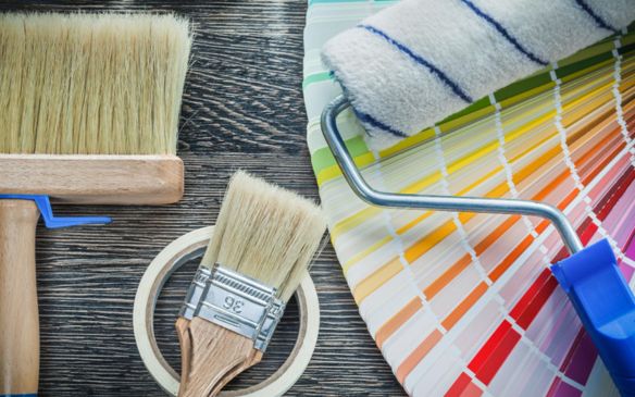 Various paint brushes and colorful paint tubes on a wooden table.