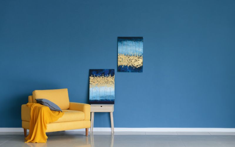 Yellow chair in front of blue painting wall with two home paintings