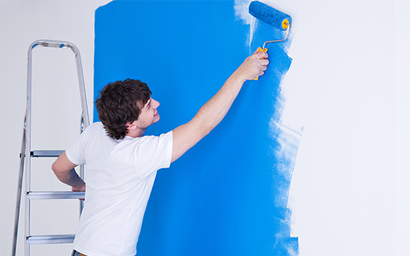 a man painting a wall with blue paint, focused and determined.